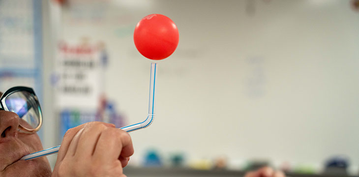 A person blows an air through a straw to levitate a ping pong ball in the air